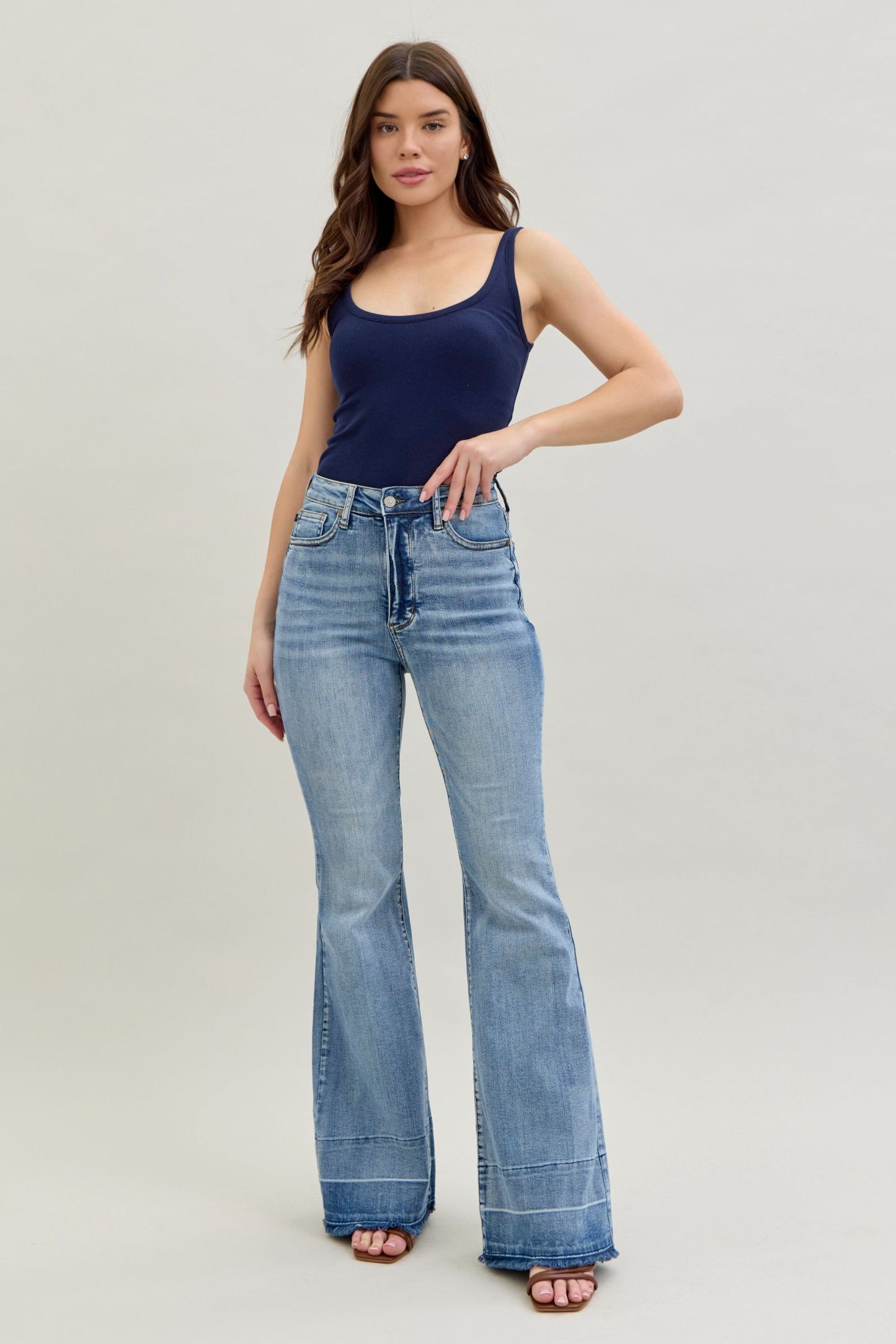 Woman wearing a navy tank top and light blue flared jeans on a plain background