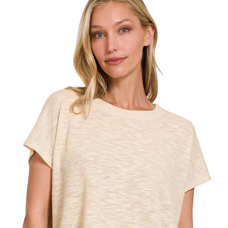 Woman wearing a sand beige top and blue jeans on a white background